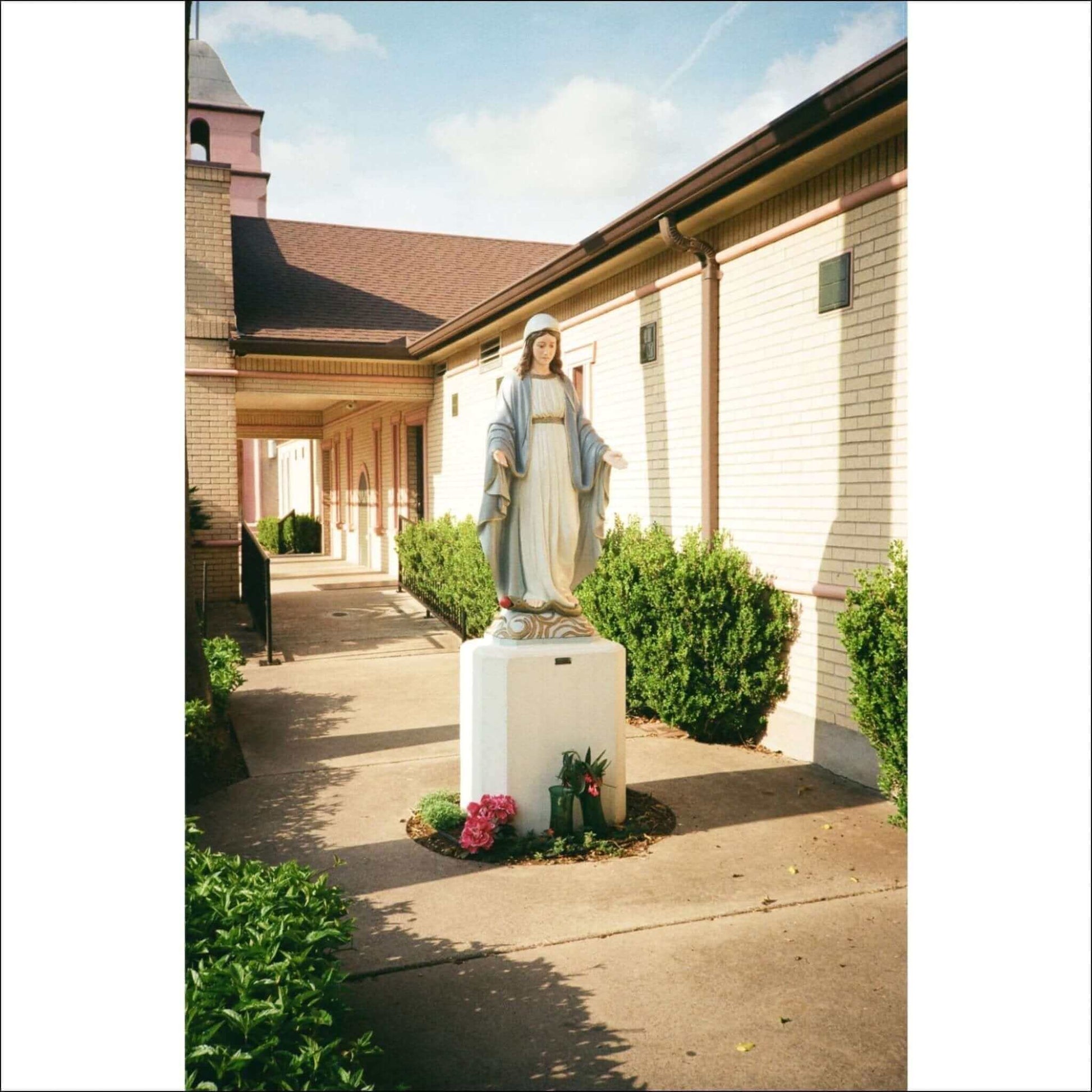 Statue of religious figure in a garden outside a brick building.