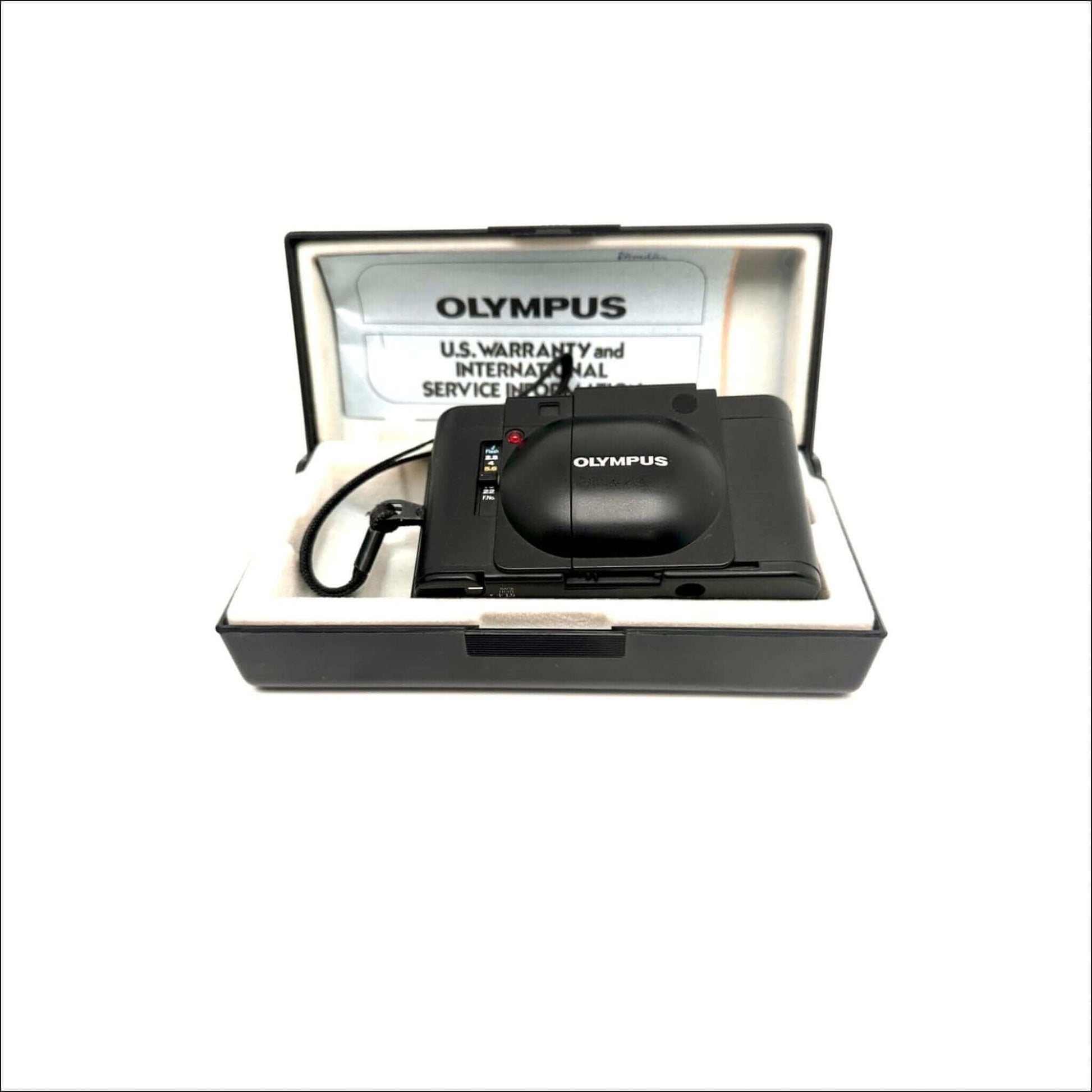 Olympus camera with warranty and service booklet in an open black and white case.