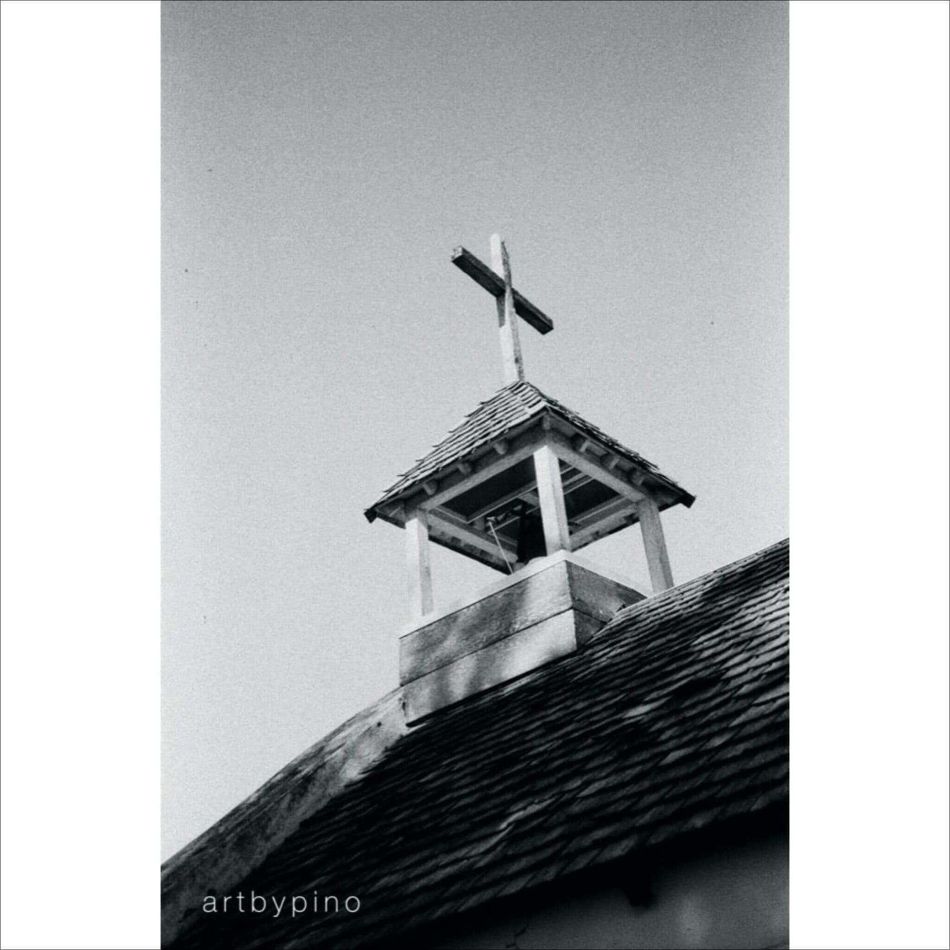 Black and white photo of a church steeple with wooden cross, roof shingles, and clear sky background by artbypino