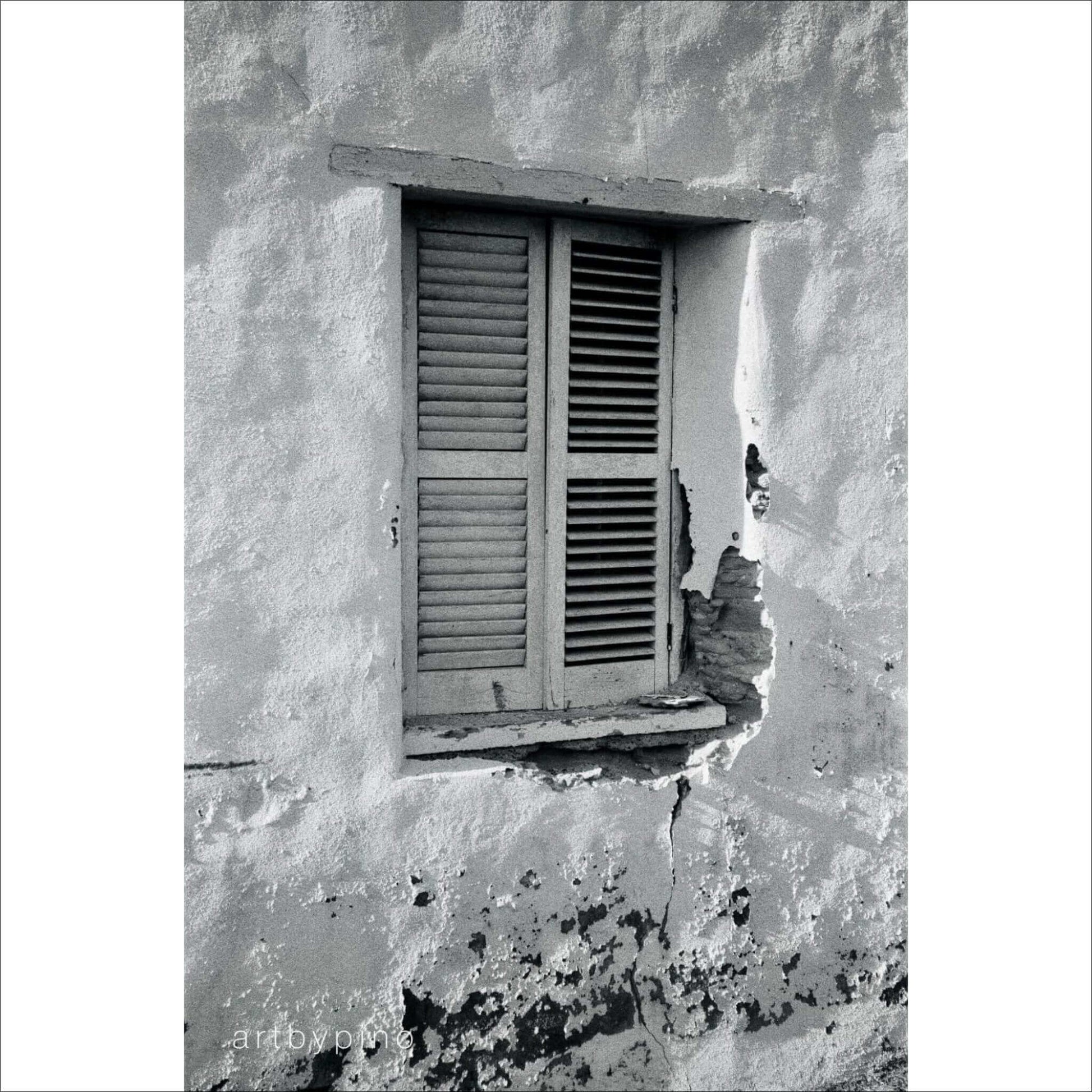 Black and white photograph of an old window with shutters on a weathered wall.