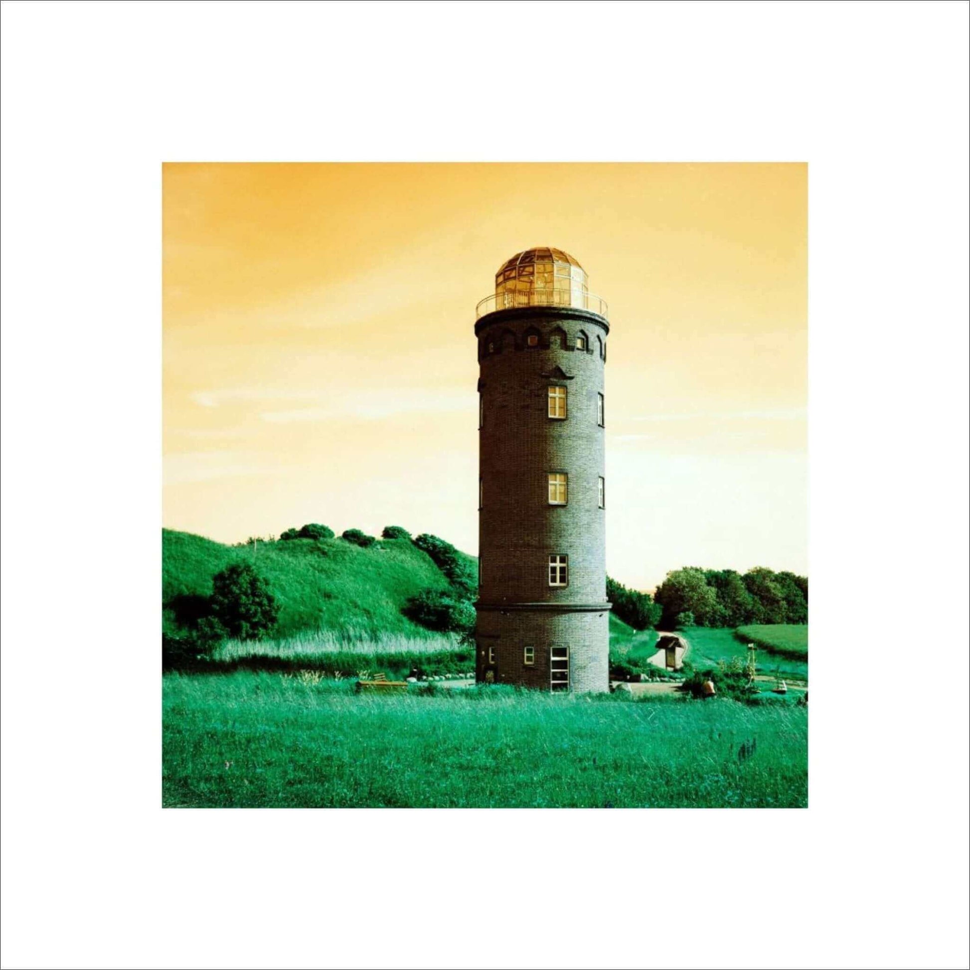 Lomography Turquoise film photo of a lighthouse against a turquoise and orange gradient sky and green landscape.